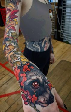 a woman with a tattoo on her arm holding up a dog's head and flowers