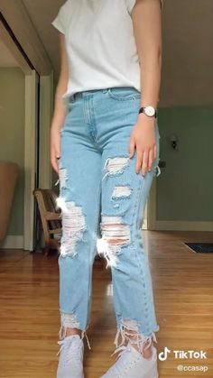 a woman standing on top of a hard wood floor wearing ripped jeans and white t - shirt