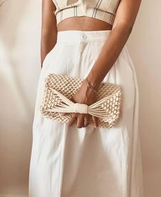 a woman wearing a white dress holding a woven purse with a knot at the bottom