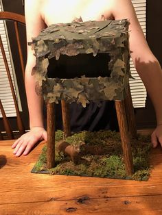 a man is sitting in front of a miniature house made out of wood and moss