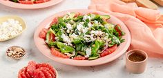 two pink plates filled with salad on top of a white marble counter next to other food items