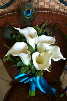 a bouquet of white calla lilies and peacock feathers sits on a chair with a blue ribbon