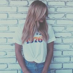 a woman standing in front of a brick wall wearing a white shirt with the word dad on it