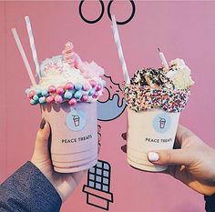 two people holding ice cream and sprinkles in front of a pink wall