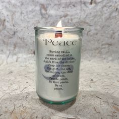 a candle that is sitting on top of a table next to a white wall with the words peace written in it