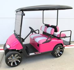 a pink and black golf cart parked in front of a white wall with the door open