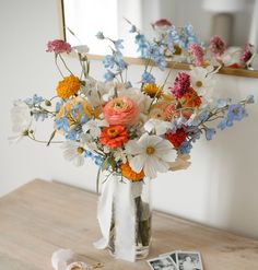 a vase filled with flowers sitting on top of a wooden table next to a mirror