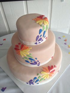 two tiered cake decorated with colorful flowers on top of a white tablecloth covered table