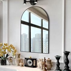 a mirror and vases on a mantle in a white room with large windows overlooking the city