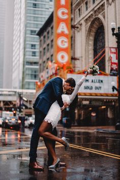 a bride and groom kissing on the street in front of chicago theatre during a rainy day