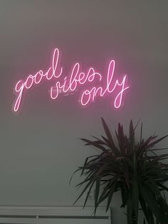 a neon sign that says good vibes only on the wall above a potted plant