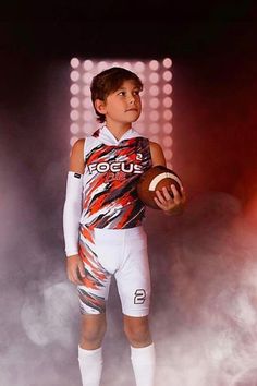 a young boy holding a football on top of a white and red field goalie's uniform