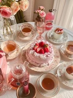 a table topped with plates and cups filled with tea next to a cake covered in strawberries