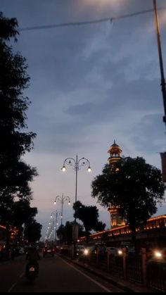 a city street at night with lights on and trees lining the sides of the road