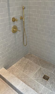 a walk in shower sitting next to a white tiled wall and floor with gold faucet