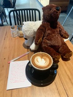 a teddy bear sitting next to a cup of cappuccino on a table