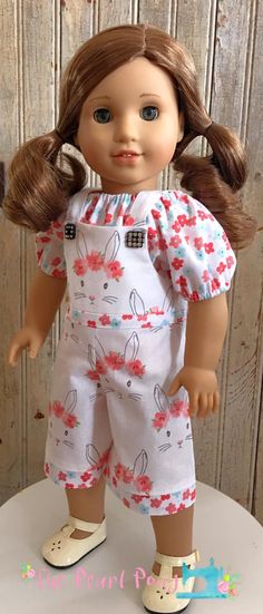 a doll with brown hair wearing white overalls and sandals on top of a table