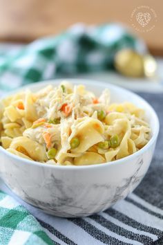 a white bowl filled with pasta and vegetables on top of a green and white table cloth