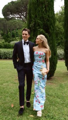 a man in a tuxedo walking next to a woman in a floral dress