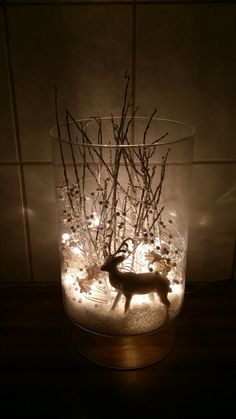 a glass vase filled with branches and lights in the shape of a deer on top of snow