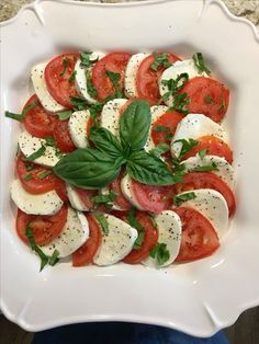 a white bowl filled with sliced tomatoes and mozzarella cheese topped with fresh basil