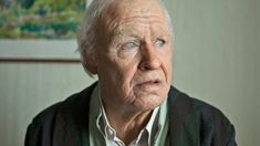 an older man sitting in front of a painting