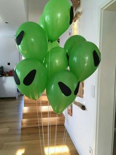 a bunch of green balloons with black eyes on them in the middle of a room