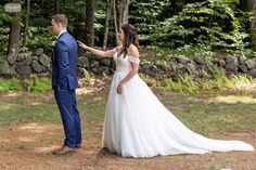 a bride and groom standing in front of some trees looking at each other while holding hands