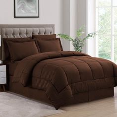 a bed with brown comforter and pillows in a room next to a plant on the floor