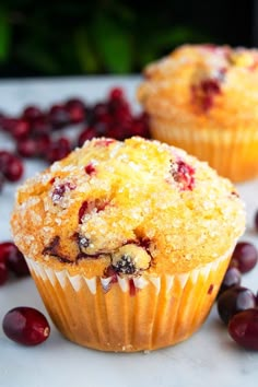 two cranberry muffins sitting on top of a white table next to some berries