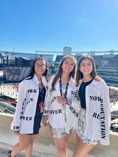 three girls in white shirts and sequin shorts posing for the camera at a football game