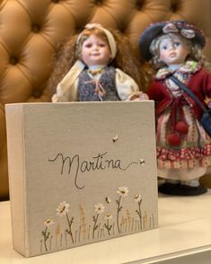 two dolls sitting on top of a table next to a sign that says marinana