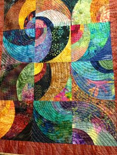 a colorful quilt is hanging on the wall in front of a tablecloth with an abstract design