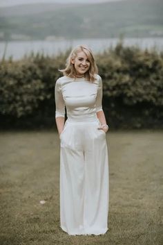 a woman standing in the grass with her hands on her hips wearing a white dress