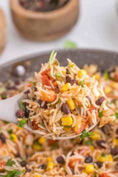 a spoonful of mexican rice and beans is being lifted from a skillet on a table