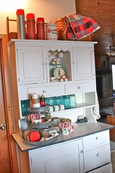 a kitchen with white cabinets and lots of christmas decorations on the top shelf in front of it