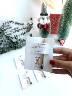 a person holding up a christmas card in front of some small trees and other decorations