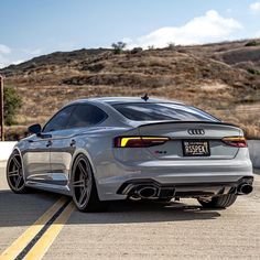 the rear end of a silver car driving down a road