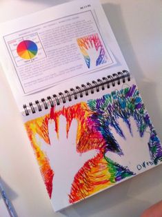 a hand is holding a notebook with colored crayons on it and the pages are open