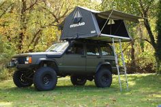 a truck with a tent attached to it parked in the grass next to some trees