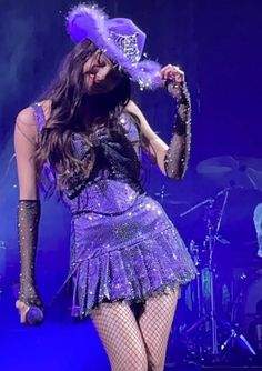 a woman in a purple dress and hat on stage