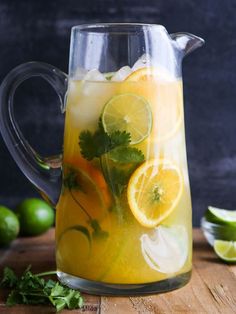 a pitcher filled with lemonade and limes on top of a wooden table