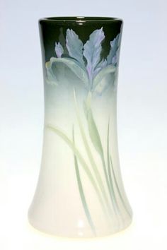 a green and white vase with flowers painted on the side, sitting in front of a white background