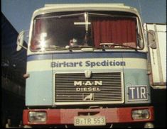 an old blue and white truck parked in front of a building with a red curtain