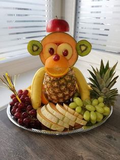 a plate with fruit and a monkey made out of bananas, grapes, apples, and pineapples