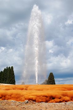 an orange substance is spewing out from the ground with trees in the background