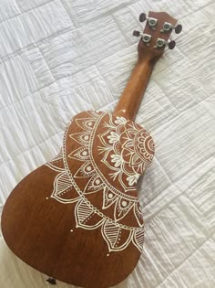 an ukulele laying on top of a bed with white and brown designs painted on it