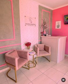 two pink chairs in front of a counter with flowers on the table next to it