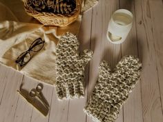 knitted mittens, eyeglasses and other items on a wooden floor next to a cup