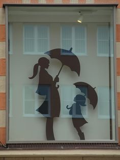 the silhouettes of two people holding umbrellas are on display in a glass window